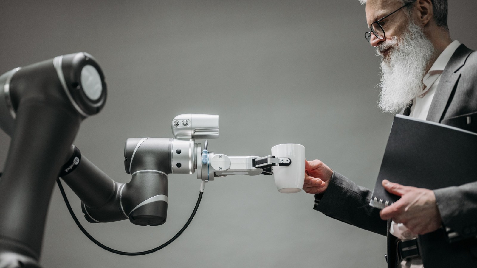 Robotska ruka drži šalicu ispred muškarca s mapom; ilustracija drugog robotskog sustava.