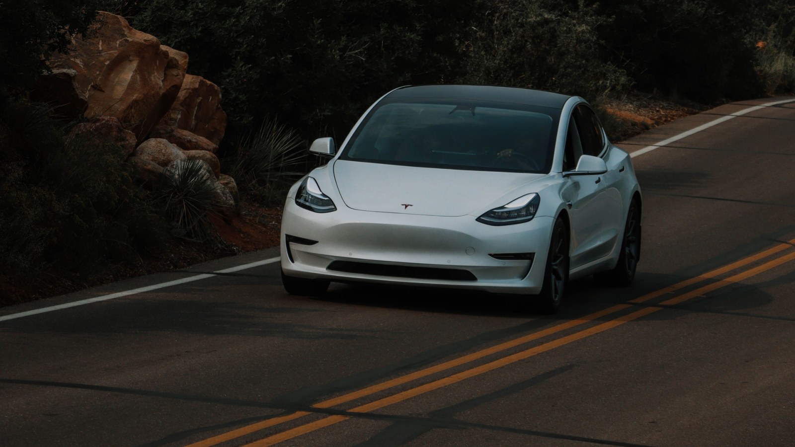 Bijela Tesla na zavojitoj cesti uz šumu i stijene; ilustracija drugog modela.