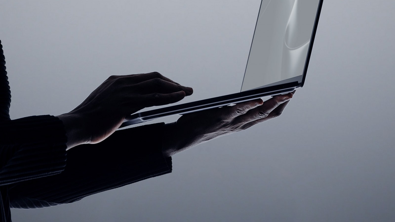 Ruke pridržavaju tanki Surface Laptop Ultra iz profila, dok kadar naglašava šasiju, zaslon i dodirnu površinu.